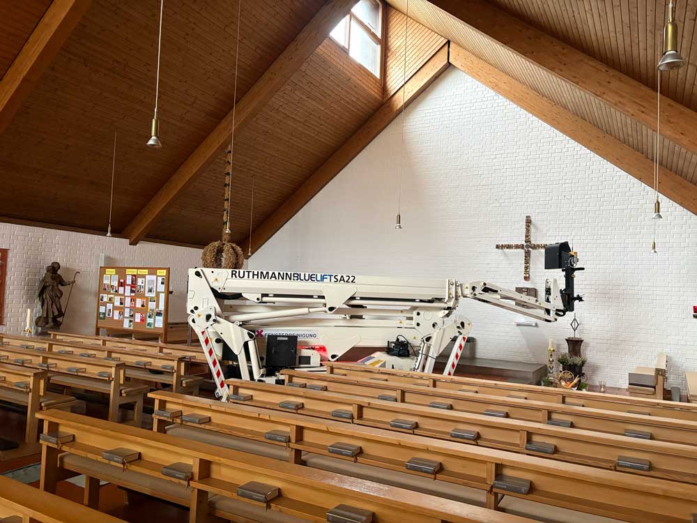 Hubarbeitsbühne zwischen den Kirchenbänken unter dem Holzdach